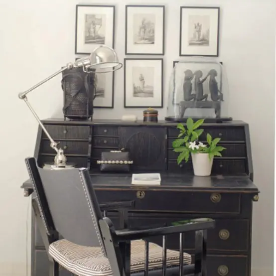 a stylish vintage home office nook with a vintage black bureau, a vintage chair with a cushion, a table lamp and a grid gallery wall