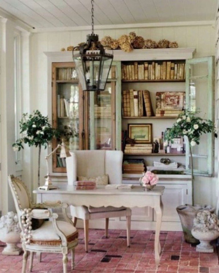 A delicate pastel vintage home office with a large bookcase with glass doors and closed storage cabinets, a vintage desk and neutral chic chairs plus a pendant lamp