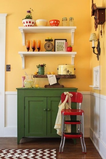 a warm yellow kitchen with white paneling and a dark green cabinet plus red touches for a bold and cool look