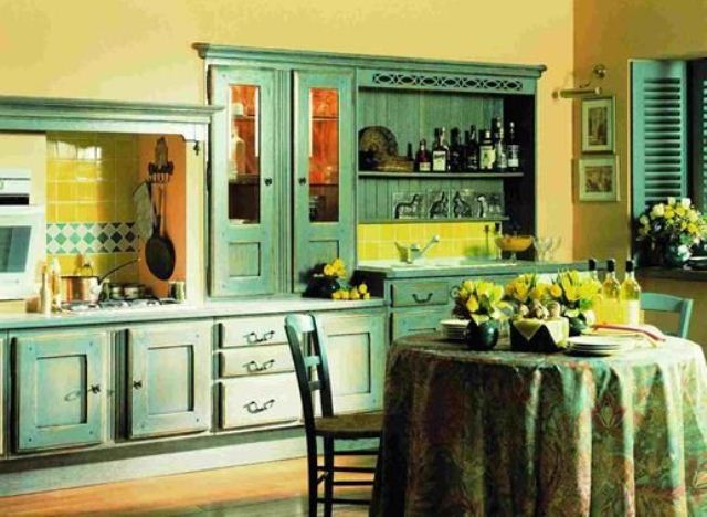 A vintage yellow kitchen with emerald cabinets, a yellow tile backsplash, a dining zone with green chairs and a green and yellow tablecloth