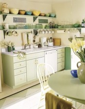 a bright vintage kitchen with light green cabinets, a green table, open shelves with green and yellow tableware
