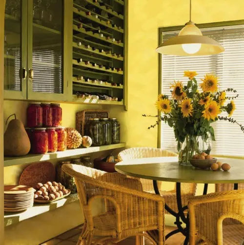 a yellow kitchen with dark green cabinets, open shelving, a yellow pendant lamp and wicker chairs