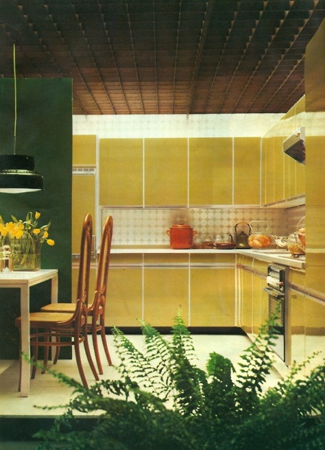 a mid-century modern kitchen mustard sleek cabinets, a printed tile backsplash and a dining zone marked with an emerald accent wall