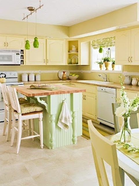 a pastel kitchen with light yellow cabinets, backsplashes and walls for a warm feel and a mint green kitchen island and green pendant lamps