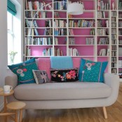 a bold hot pink wall, turquoise shades and matching colorful pillows make this living room feel like summer