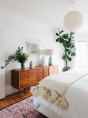a welcoming boho meets mid-century modern bedroom with boho rugs, a warm-colored dresser and much potted greenery