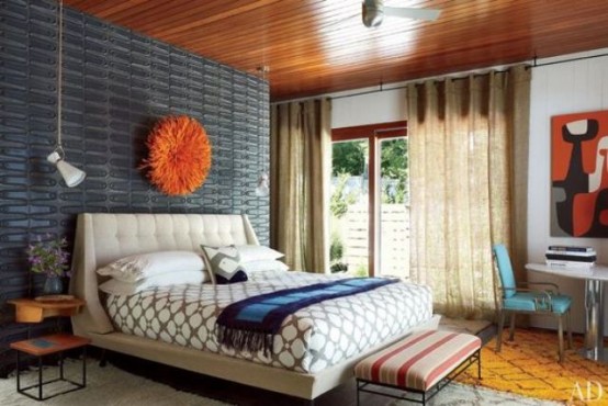 a colorful mid-century modern bedroom with a grey metal wall, a neutral bed, a striped stool and a turquoise leather chair