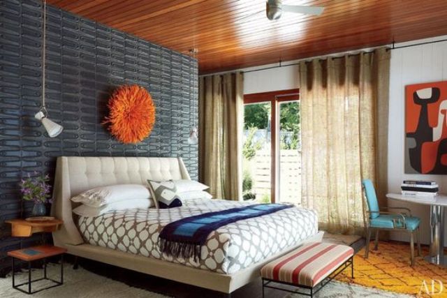 A colorful mid century modern bedroom with a grey metal wall, a neutral bed, a striped stool and a turquoise leather chair