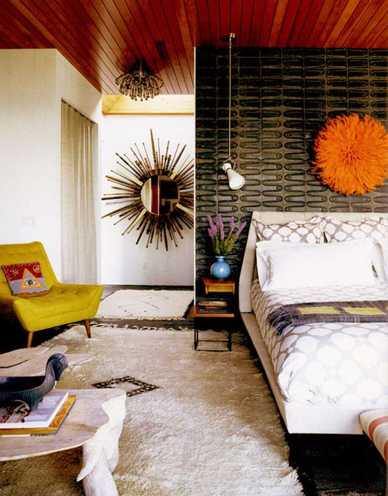 A bright mid century modern bedroom with a cathcy black wall, a mustard chair, a fluffy rug and an orange decoration over the bed
