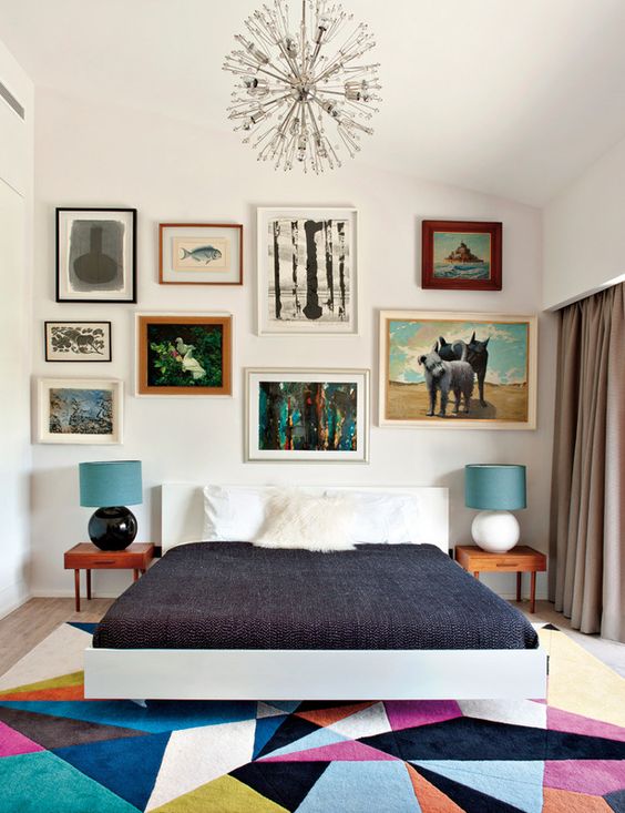 A colorful mid century modern bedroom with a bright geometric rug, a bed, laconic nightstands and an eclectic gallery wall