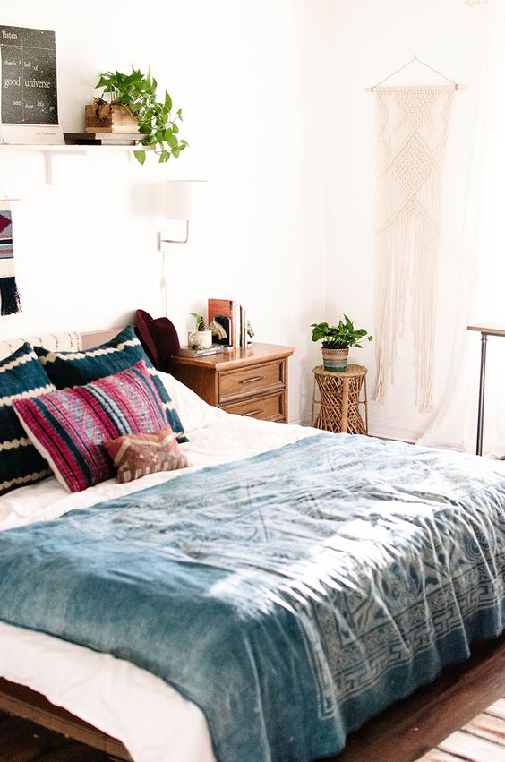 A boho meets mid century modern bedroom with rich stained furniture, a macrame hanging and potted plants