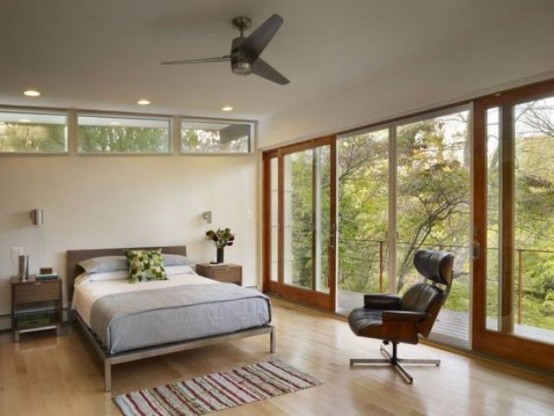 a mid-century modern bedroom with a fully glazed wall, some small windows, a bed and a large comfy leather chair