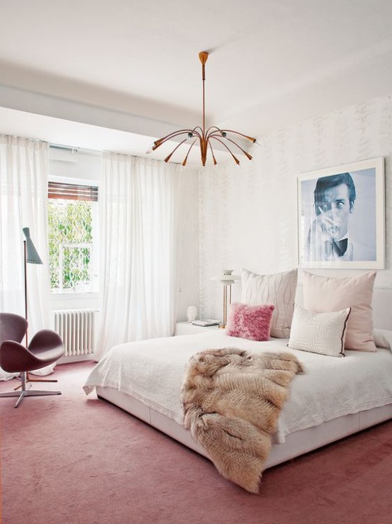 a bright mid-century modern bedroom with a pink rug and chair, a copper chandelier, a large bed and an artwork