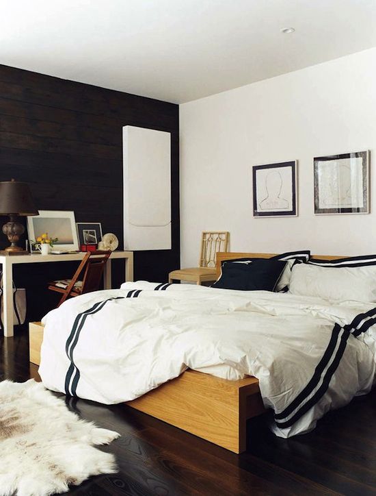 a monochromatic mid-century modern bedroom with a wooden bed and console plus a statement black wall