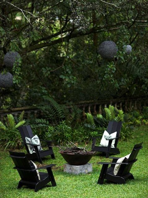 A beautiful and all green outdoor space with a fire bowl, black chairs, printed pillows and black pendant lamps