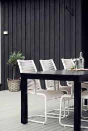 a minimalist outdoor dining space with a black dining table, white metal chairs, a potted tree and some greenery is chic