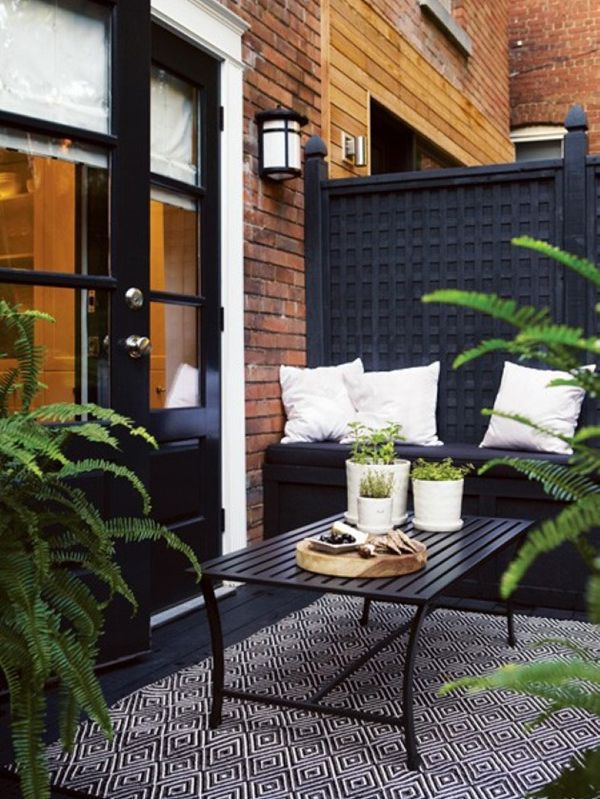 A Nordic balcony with a black wall, a black built in bench and a wooden table, a printed chair and potted greenery to refresh the space
