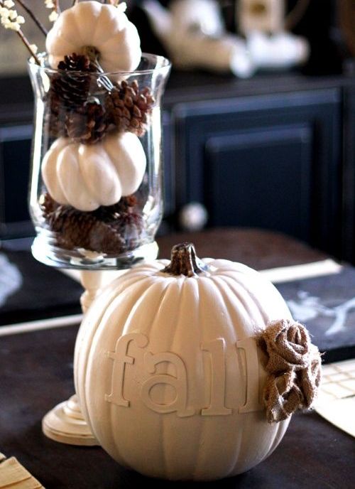 a Nordic fall centerpiece of a fake pumpkin with letters and a burlap flower and a vase with pinecones and mini pumpkins