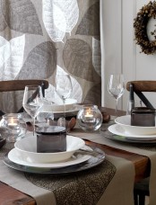 a Nordic fall tablescape made in greys, with a leafy curtain, candles, a wreath and some greyish textiles