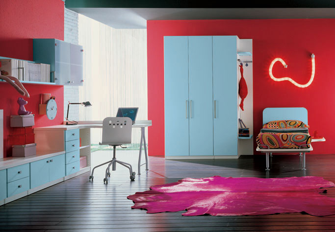A cool teen bedroom with red walls, blue furniture, a neon sign, a brigth rug and bold printed bedding is super cool