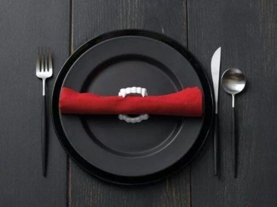 simple styling with black plates, black cutlery and a red napkin with vampire teeth for a modern Halloween party