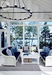 a stylish nautical sunroom with white wicker furniture, navy upholstery and pillows and a vintage chandelier