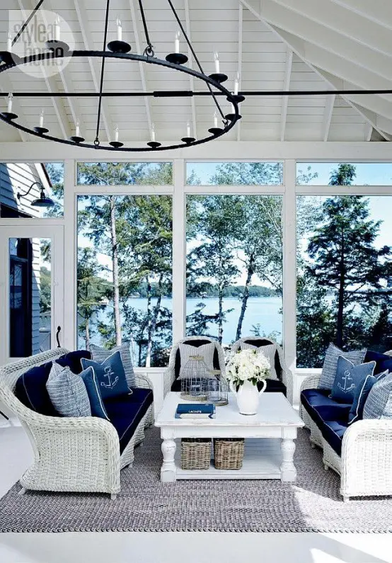a stylish nautical sunroom with white wicker furniture, navy upholstery and pillows and a vintage chandelier