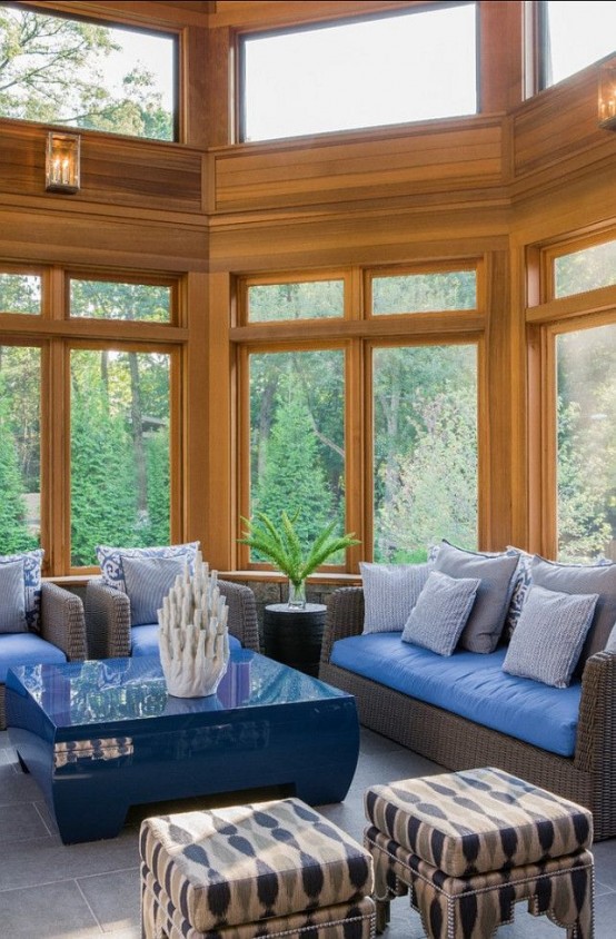 a bold blue beachy sunroom with dark woven furniture and blue upholstery, a blue table and corals plus printed stools