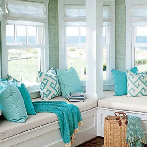 A beach sunroom with built in benches, tiffany blue and printed pillows plus a cool coastal view