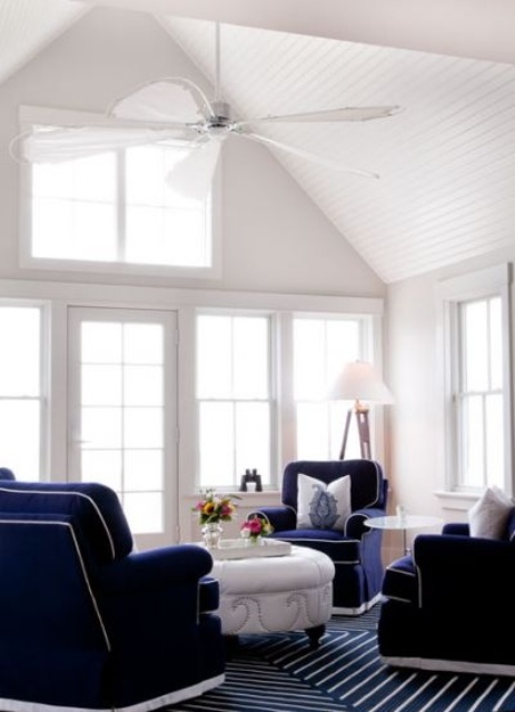 a vintage nautical sunroom with navy carpet floors, navy furniture,a white table and much natural light