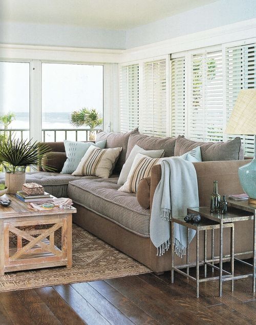 a beach sunroom with chocolate brown and light blue furniture, wooden and metal tables and potted greenery