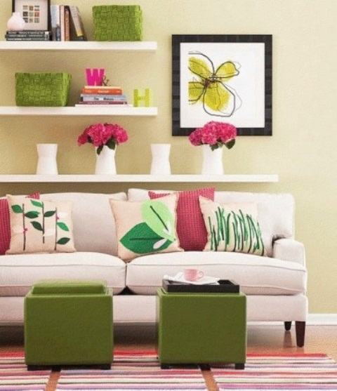 a bright and cool living room with pale yellow walls, open shelves, bright artworks and accessories, embroidered pillows and green ottomans