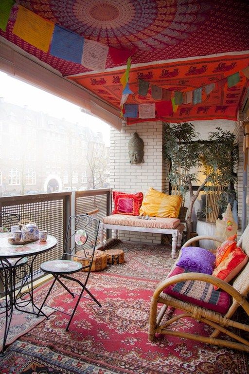 a super colorful boho balcony with a bold pink and orange ceiling, colorful garlands, a bold boho rug, rattan furniture with colorful pillws and a small table and a chair