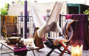 a colorful boho balcony with folding chairs with bright covers, a table, a hammock with lots of pillows and blankets and a large candle holder is very inviting