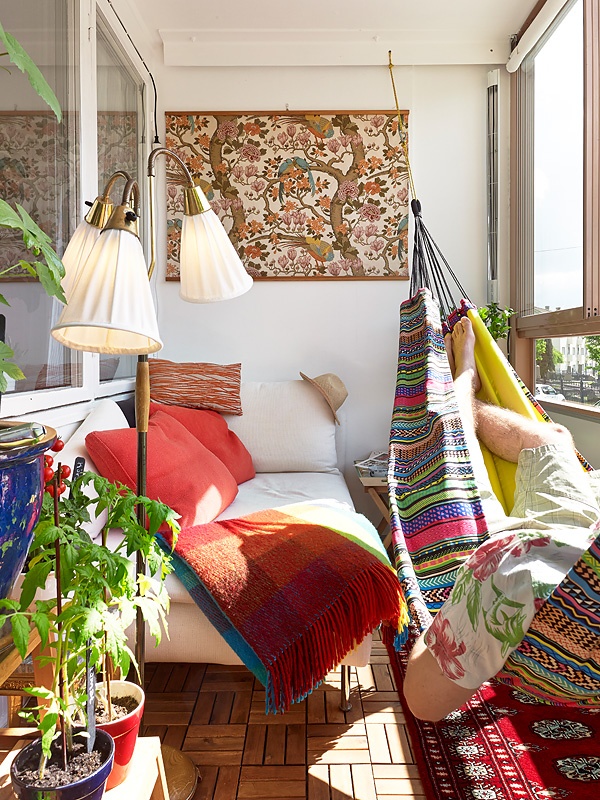 A mid century modern meets boho balcony with a bright printed rug, a colorful boho hammock with pillows, a bold artwork and a neutral daybed with colorful pillows