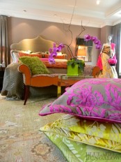 a beautiful earthy bedroom done in taupe, orange, grey and green and accented with neon pillows, an orange printed bench with bright pillows and colorful blooms
