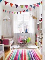 a neutral Scandinavian kids’ bedroom made bright with super colorful textiles – rugs, bedding, buntings and a white storage unit with bright books and toys