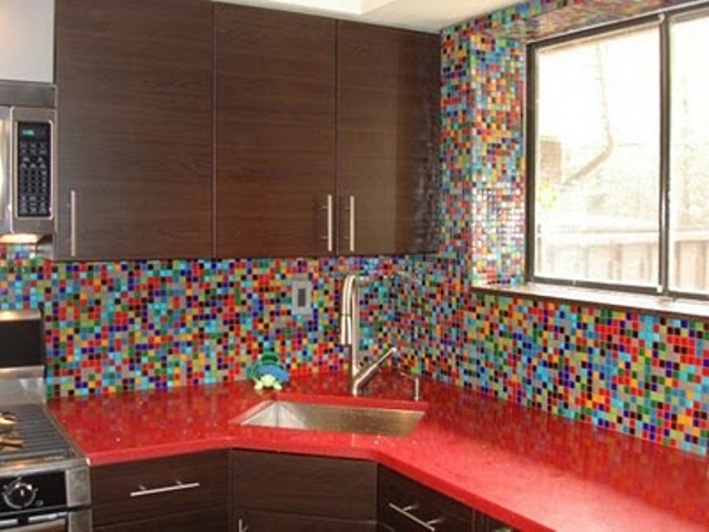 A rich stained kitchen with bold red countertops and a colorful mosaic tile backsplash and walls that accents the space and makes it non boring