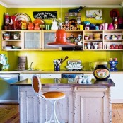 a fun and colorful kitchen with mustard walls, open and closed storage units, a shabby chic kitchen island and stools plus lots of decor and accessories
