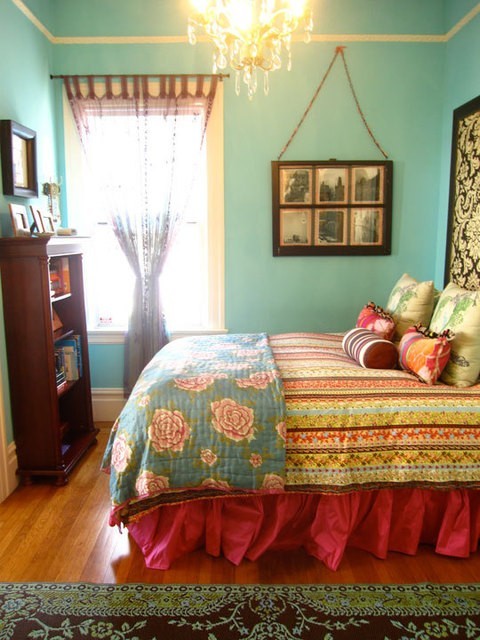 a turquoise bedroom with a dark stained bookcase, a bed with colorful bedding, bright artwork and other types of decor