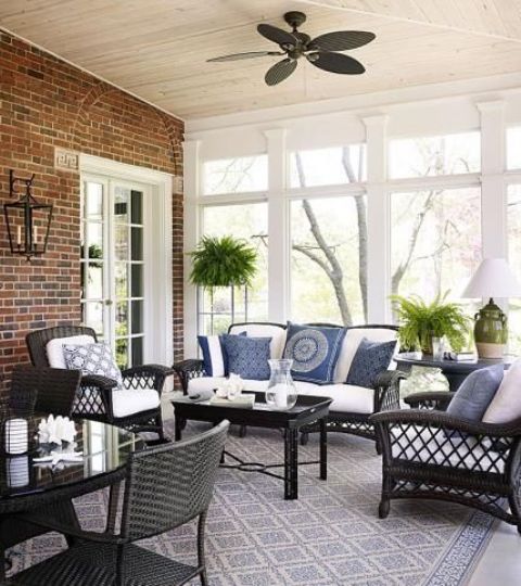 A mid century modern porch with black wicker furniture with white and blue upholstery, potted greenery and table lamps and a cool view