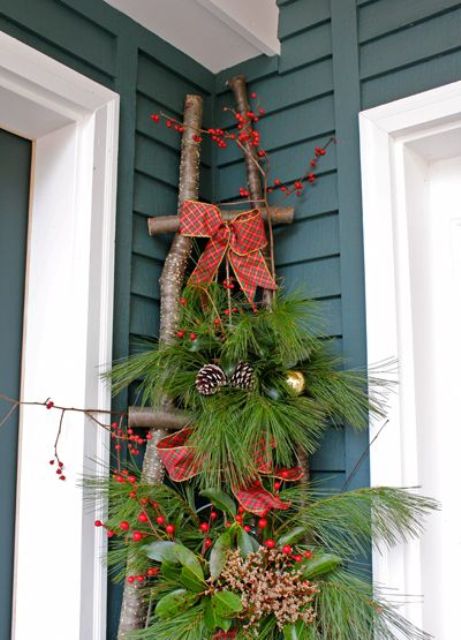 a ladder of branches, fir branches, pinecones, berries, red bows and metallic ornaments for rustic front porch decor