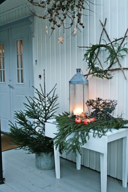 A non decorated Christmas tree in a bucket, fir branches on the table, pomegranates, a lantern and a fir wreath with sticks