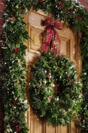 a lush greenery and berry garland framing the door and a matching wreath with a bow on top for a gorgeous Christmas front porch
