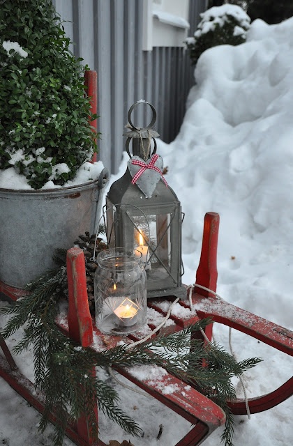 a red  sleigh with candle lanterns, a plant in a bucket and some fir branches is a lovely and chic idea for outdoor Christmas decor with a rustic feel