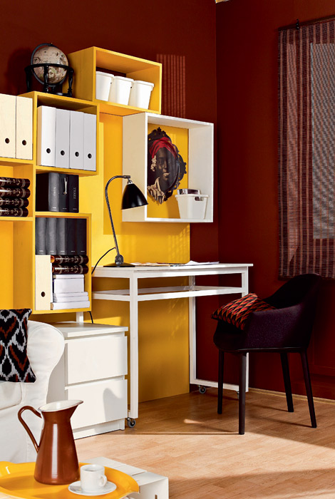 Compact home office in a living room with a bright yellow storage wall.