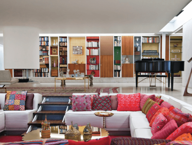 A bold modern living room with a built in conversation pit with a white sofa, colorful and printed pillows, gold coffee tables that add chic and glam to the space