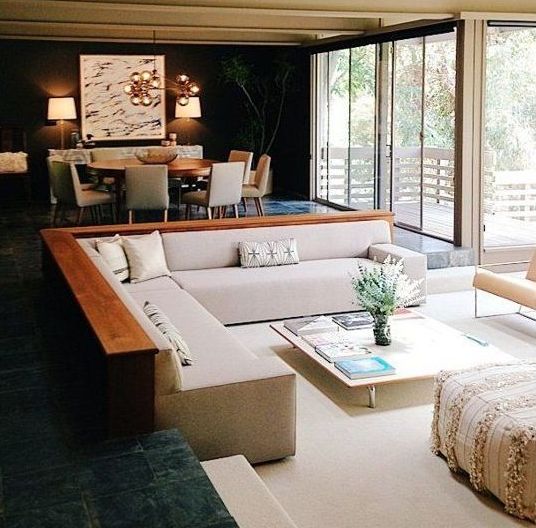 a modern living room done in dark shades but with a neutral creamy conversation pit, with a low coffee table and lots of Moroccan pillows