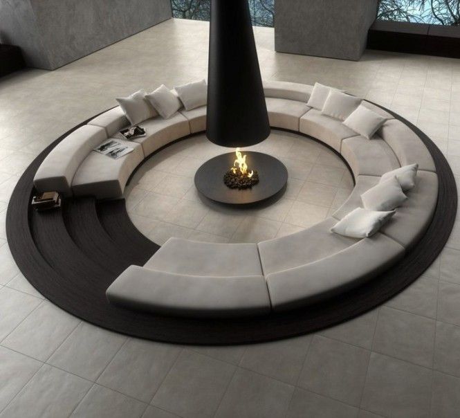 A neutral minimalist living room done with concrete, with a round conversation pit with an open fireplace in the center and a sofa all around it