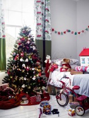 a neutral kid’s room decorated for Christmas wiht a beautiful Christmas tree, garlands and banners, bold color block curtains and Christmas-inspired plush toys